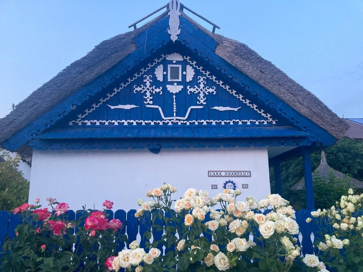 Fatada Casa Soarelui Murighiol cu acoperis stuf, fronton albastru decorat si trandafiri