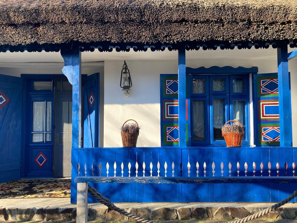 Prispă traditionala cu pereti albi, tamplarie albastra si cosuri decorative din rachita